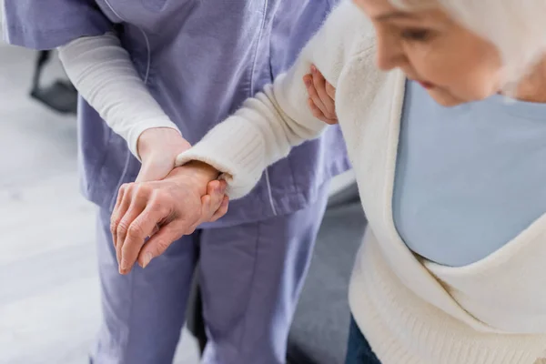 Visión parcial de la enfermera de apoyo a la mujer anciana, borrosa primer plano - foto de stock