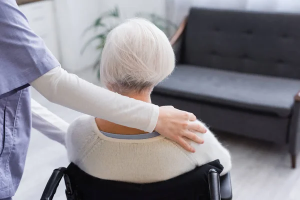 Vista posteriore della donna anziana disabile vicino all'assistente sociale che abbraccia la spalla — Foto stock
