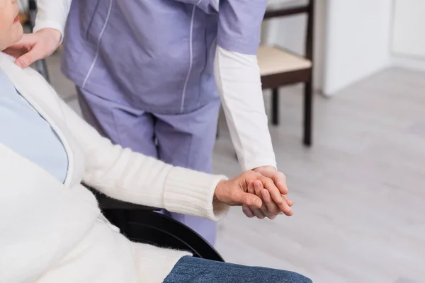 Vue partielle du travailleur social tenant la main et touchant l'épaule d'une femme âgée handicapée — Photo de stock