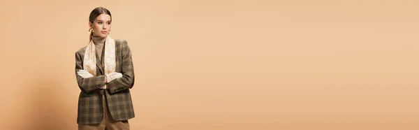 Femme tendance en blazer marron et gants blancs posant les bras croisés sur beige, bannière — Photo de stock