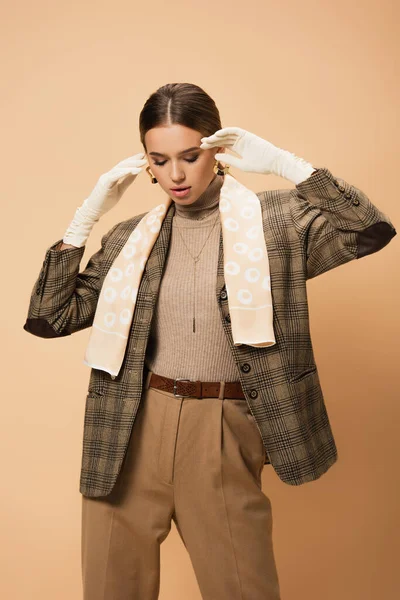 Elegante mujer en chaqueta a cuadros y guantes blancos posando sobre fondo beige - foto de stock