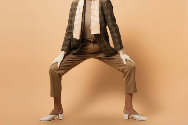 Ausgeschnittene Ansicht einer modischen Frau in Blazer, Hose, weißen Handschuhen und Schuhen, die auf beige posiert — Stockfoto