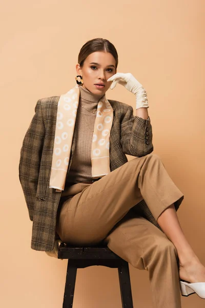 Young woman in fashionable blazer and pants looking at camera while sitting on beige — Stock Photo