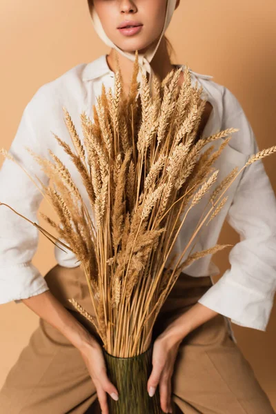 Cropped view of young woman in white shirt holding wheat spikelets isolated on beige — Stock Photo