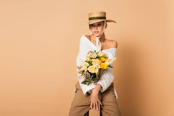 Молодая женщина в соломенной шляпе держит букет цветов на бежевом — стоковое фото