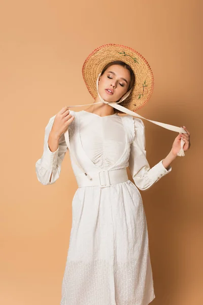 Young woman in white dress and straw hat holding ribbons on beige — Stock Photo