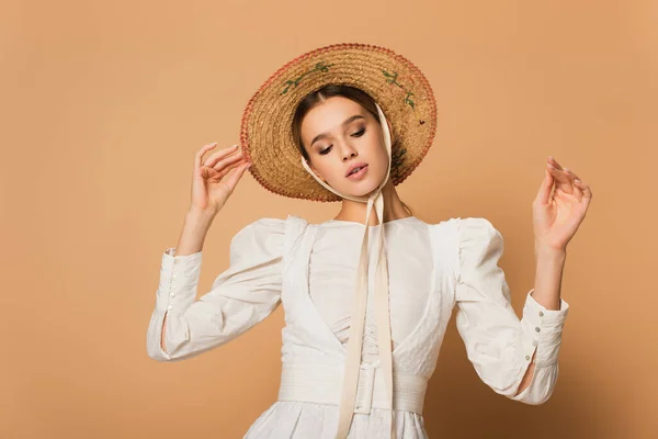 Giovane donna in abito bianco regolazione cappello di paglia su beige — Foto stock