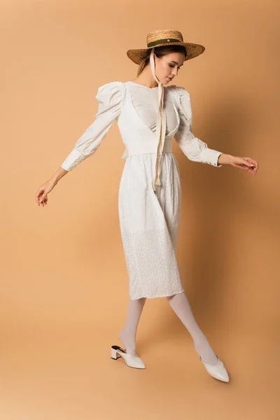 Pleine longueur de jeune femme en robe blanche et chapeau de paille posant sur beige — Photo de stock