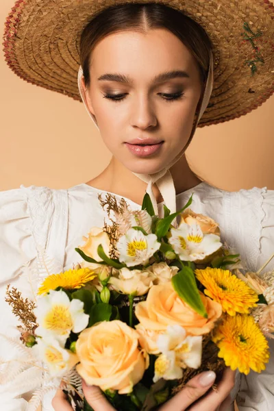 Young woman in dress looking at bouquet of flowers on beige — Stock Photo
