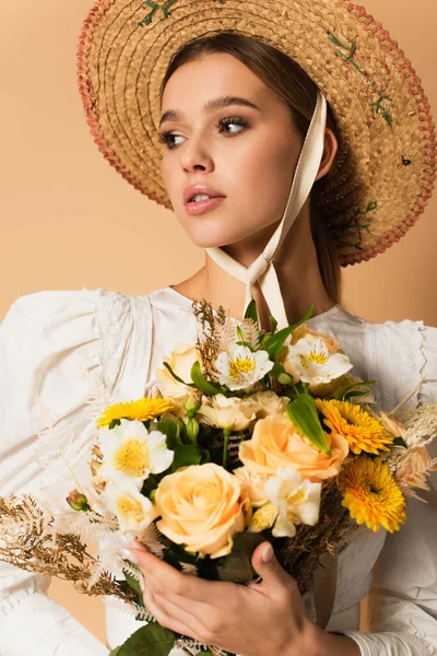 Молода жінка в солом'яному капелюсі тримає букет квітів на бежевому — Stock Photo