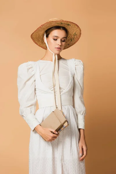 Young woman in straw hat holding books on beige — Stock Photo