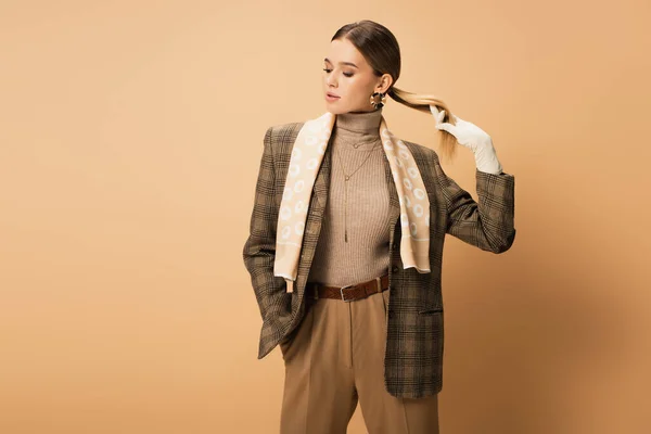 Stylish woman in checkered blazer, pants and white gloves posing with hand in pocket on beige — Stock Photo