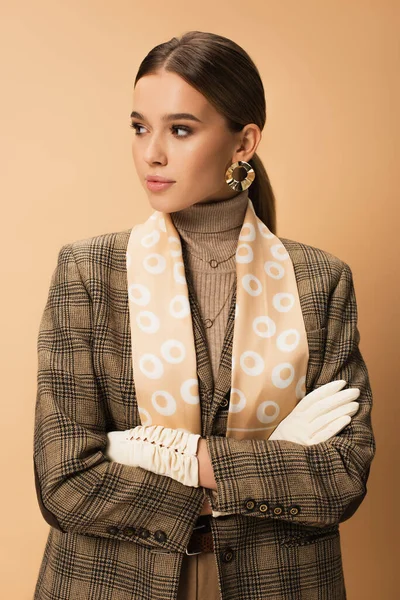 Stylish woman in checkered blazer, pants and white gloves posing with crossed arms on beige — Stock Photo