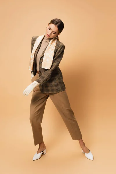 Comprimento total da mulher na moda em blazer xadrez e calças posando no bege — Fotografia de Stock
