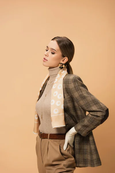 Mulher na moda em blazer xadrez, calças e luva branca posando no bege — Fotografia de Stock