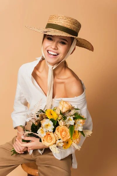 Jovem alegre em chapéu de palha segurando buquê de flores diferentes em bege — Fotografia de Stock