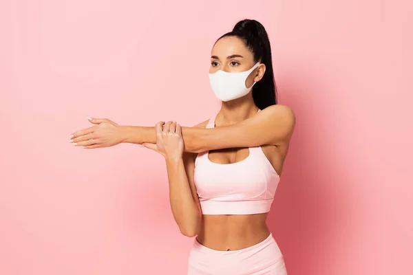 Молодая спортсменка в медицинской маске разогревается на розовом — стоковое фото