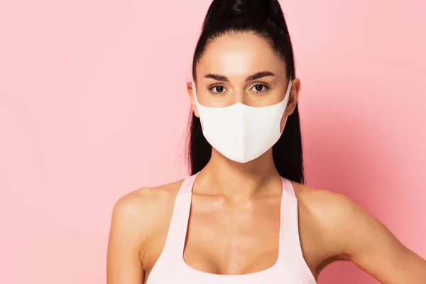 Junge Sportlerin mit medizinischer Maske blickt auf rosa Kamera — Stockfoto