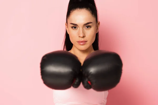 Giovane donna forte in abbigliamento sportivo e guanti da boxe sfocati su rosa — Foto stock