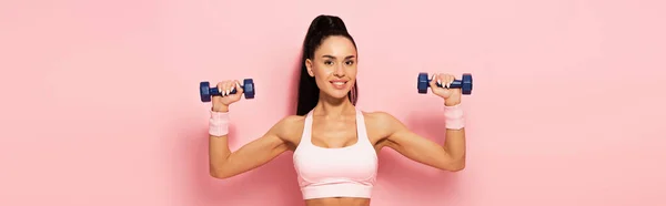 Alegre joven deportista haciendo ejercicio con mancuernas en rosa, pancarta - foto de stock