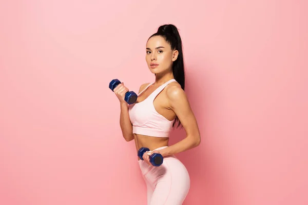 Young sportswoman working out with dumbbells on pink — Stock Photo