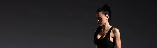 Молодая спортсменка в черной спортивной одежде, стоящая на темном фоне, баннер — стоковое фото