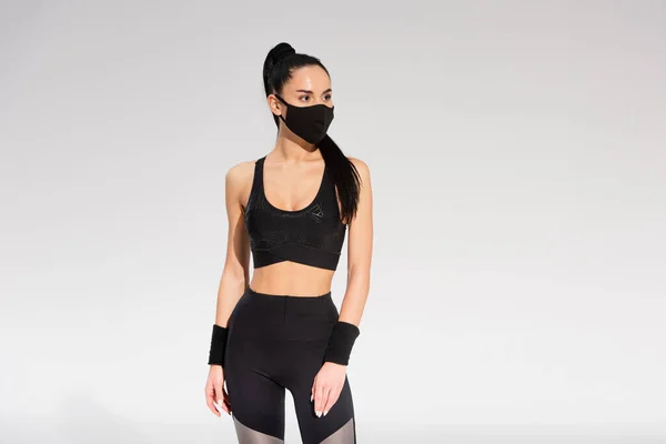 Young sportswoman in sportswear and black protective mask standing on grey — Stock Photo