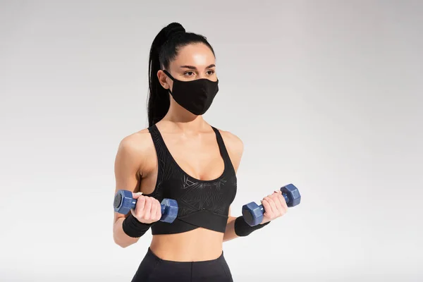 Sportiva in maschera protettiva nera che esercita con manubri su grigio — Foto stock