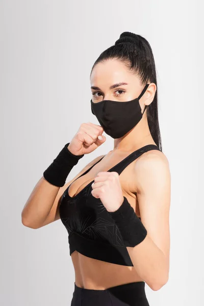 Joven luchador en ropa deportiva y máscara protectora negra con puños cerrados en gris - foto de stock