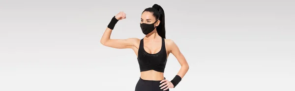 Junge Frau in Sportbekleidung und schwarzer Schutzmaske, die Muskeln isoliert auf Grau zeigt, Banner — Stockfoto