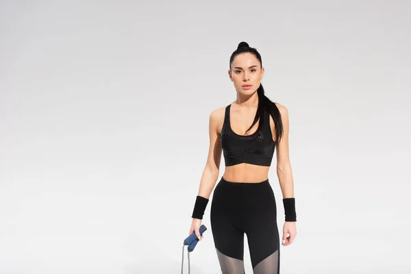 Молодая спортсменка держит скакалку на сером — стоковое фото