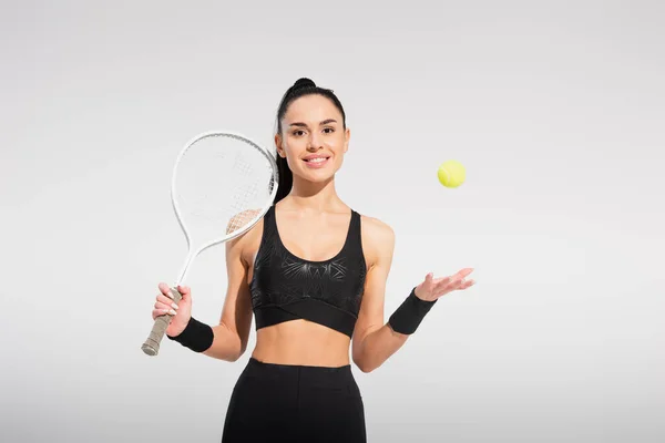 Young sportswoman holding tennis racket and throwing ball on grey — Stock Photo