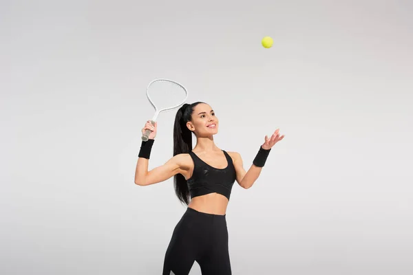 Happy sportswoman holding tennis racket and throwing ball while playing on grey — Stock Photo