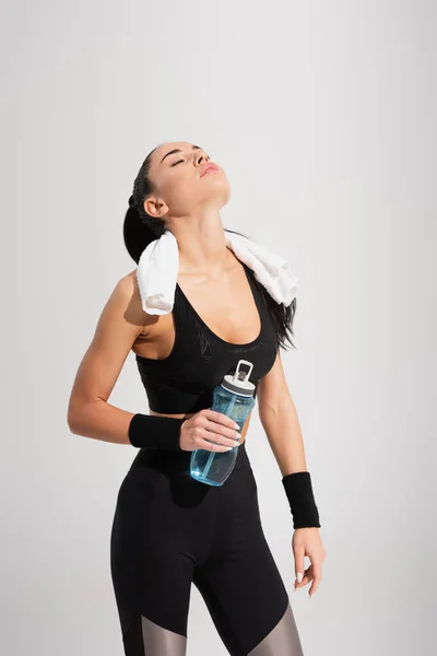 Jeune sportive aux yeux fermés tenant une bouteille de sport isolée sur fond gris — Photo de stock