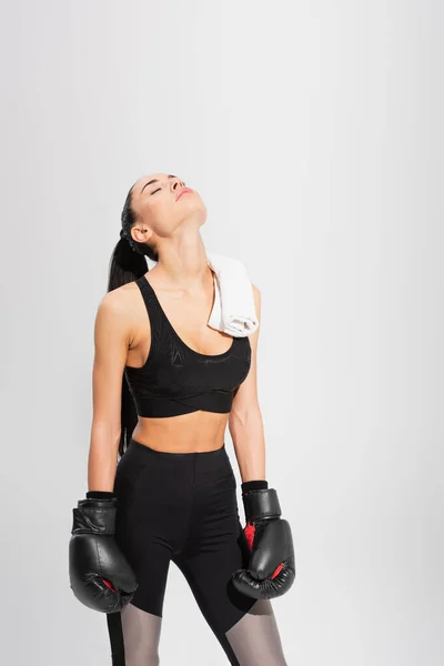 Brunette young sportswoman with closed eyes in boxing gloves isolated on grey — Stock Photo