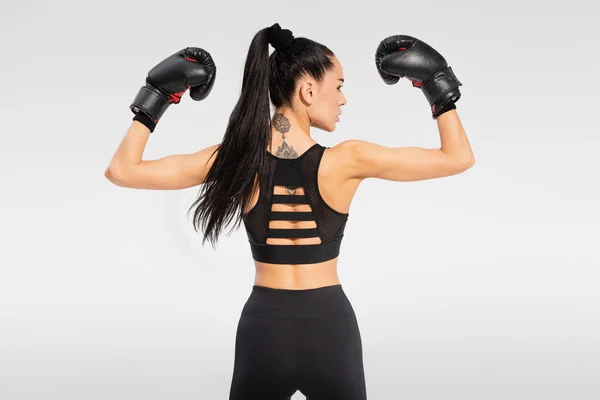 Vista posterior de la deportista tatuada en guantes de boxeo aislados en gris - foto de stock