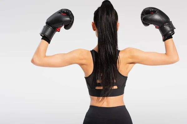 Back view of brunette young sportswoman in boxing gloves isolated on grey — Stock Photo