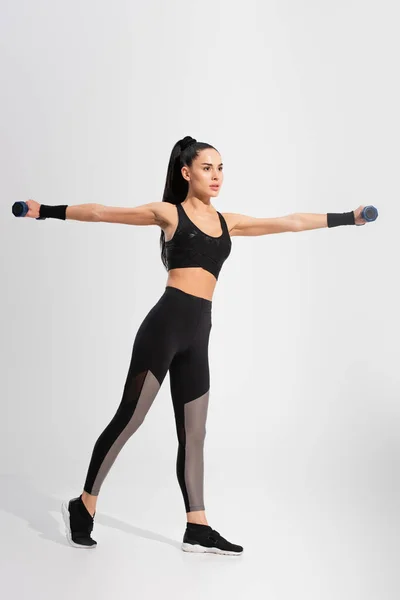 Kräftige junge Sportlerin in Sportbekleidung beim Training mit Kurzhanteln auf grau — Stockfoto