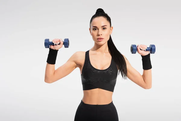 Strong young sportswoman exercising with dumbbells isolated on grey — Stock Photo