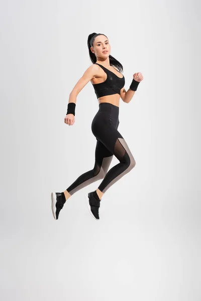 Full length of young woman in sportswear levitating on grey — Stock Photo