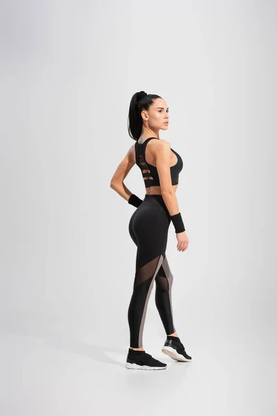 Full length of tattooed and brunette sportswoman posing on grey — Stock Photo