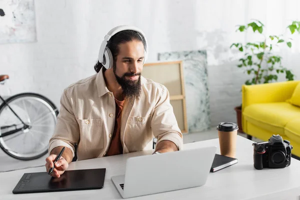 Hispanic designer in headphones working near laptop, graphic tablet and digital camera — Stock Photo