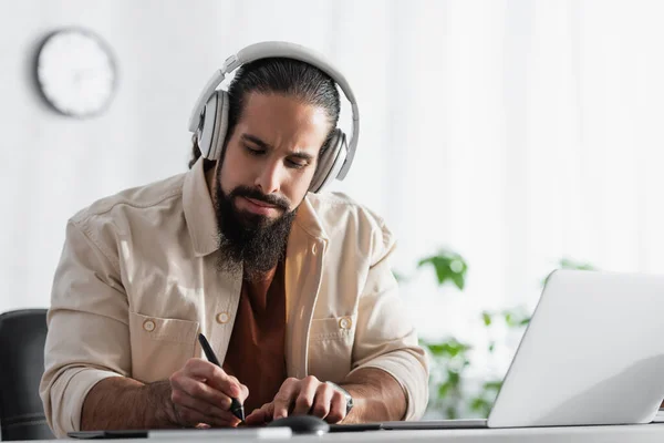 Hispanische Designerin in Kopfhörer-Zeichnung mit Stift in der Nähe von verschwommenem Laptop — Stockfoto