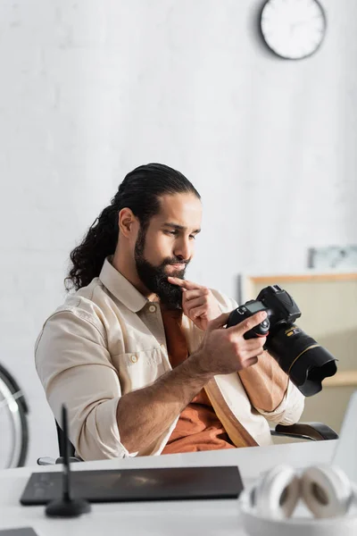 Pensoso ispanico uomo toccare la barba mentre guardando fotocamera digitale vicino tablet grafico offuscata — Foto stock