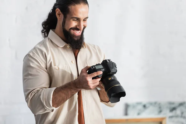 Heureux homme hispanique souriant tout en regardant appareil photo numérique moderne à la maison — Photo de stock