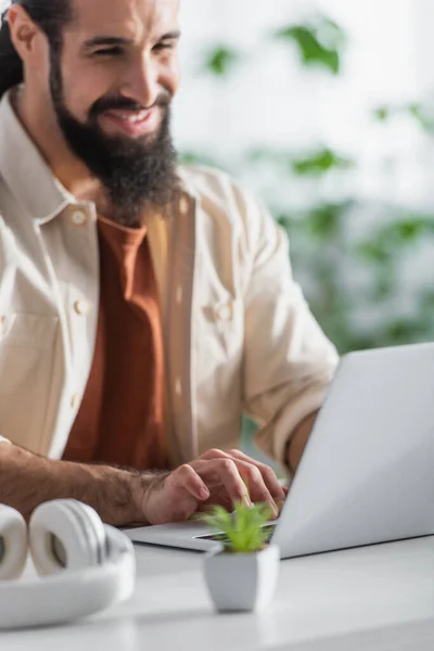 Freelancer hispânico borrado sorrindo enquanto digita no laptop em casa — Fotografia de Stock