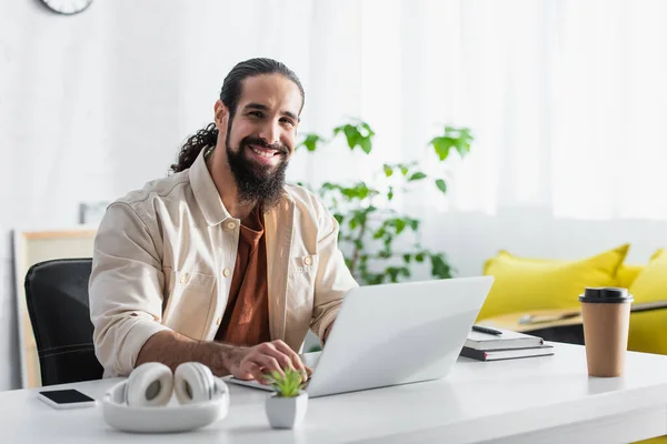Happy latin freelancer looking at camera while working on laptop at home — Stock Photo