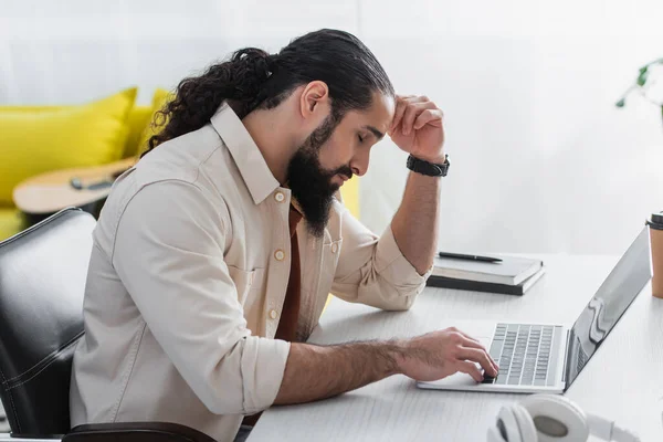 Side view of tired hispanic freelancer sitting at work desk near laptop at home — Stock Photo