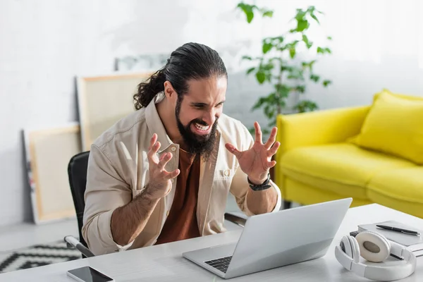 Irritado latino freelancer gesto mientras mira el ordenador portátil - foto de stock