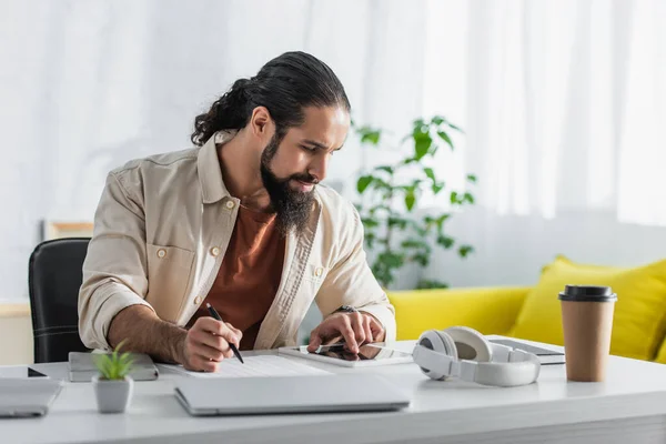 Freelancer latino barbudo usando tablet digital enquanto trabalha com documentos em casa — Fotografia de Stock